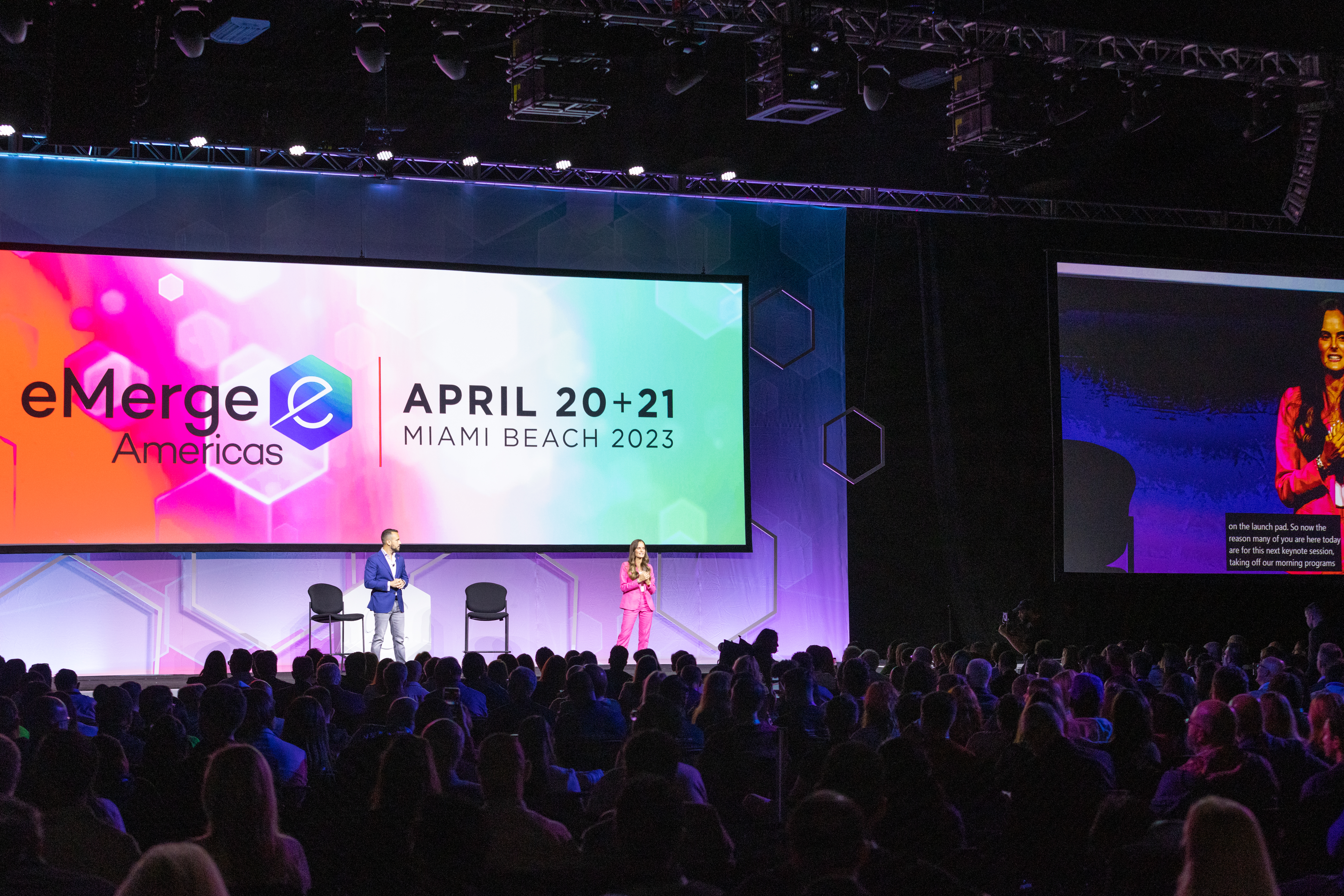 Two speakers onstage in front of a large crowd at eMerge Americas 2023.